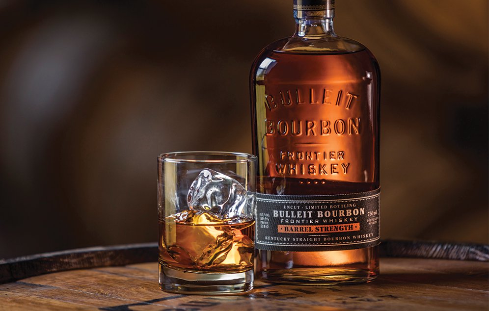 A bottle of Bulleit Bourbon placed on a rustic wooden surface, alongside a glass filled with the amber liquid, highlighting the rich color and distinctive label of the bourbon