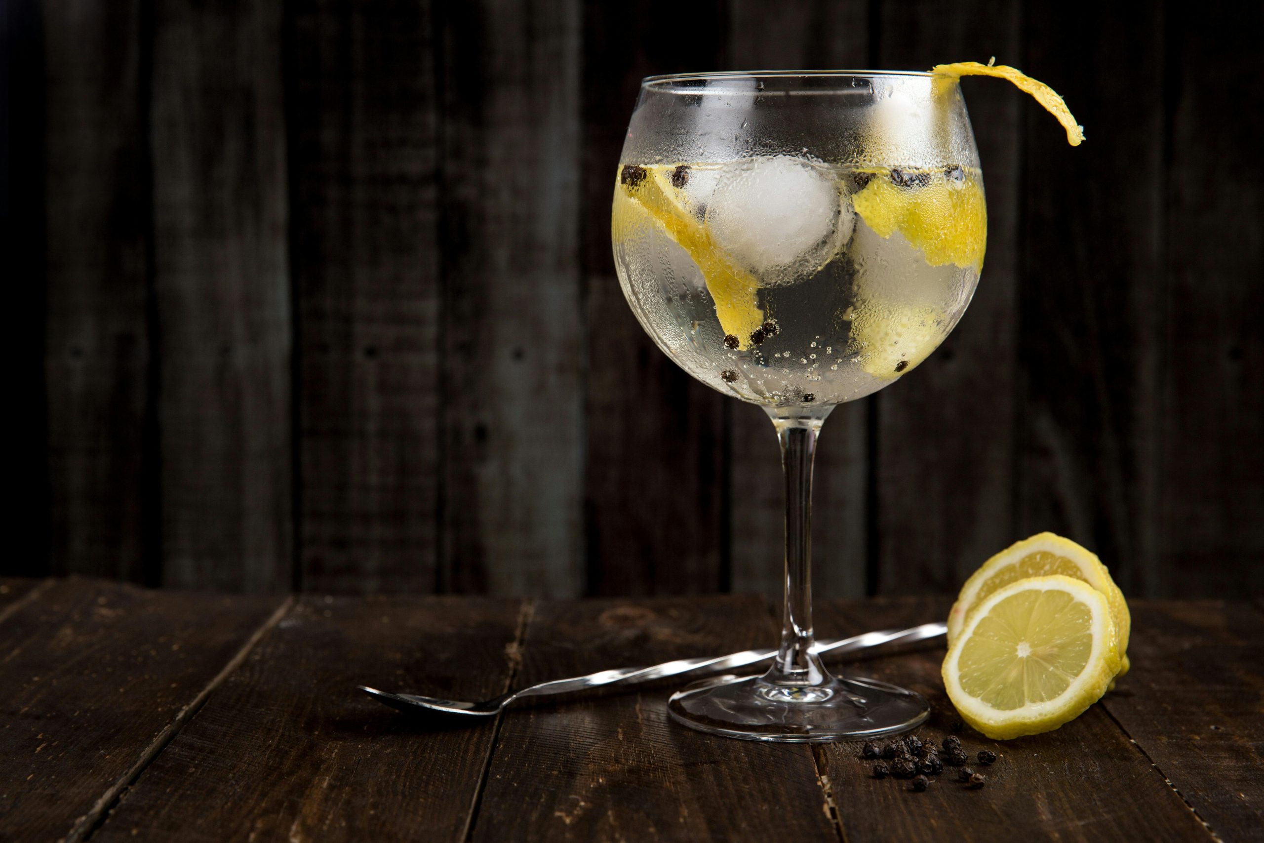 Glass of gin and tonic with a slice of lemon inside and a fresh lemon on the table, showcasing a citrusy and refreshing twist on the classic cocktail. Perfect for those who enjoy a zesty gin experience